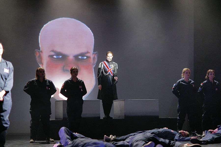 CGI John Bull head appears on a projections screen behind actors playing other characters in Oh, What a Lovely War!
