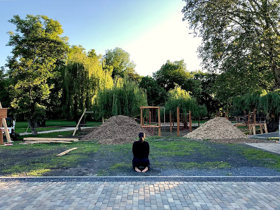 Sharon Reshef, dressed in black, kneels on the grass with her back to the camera.