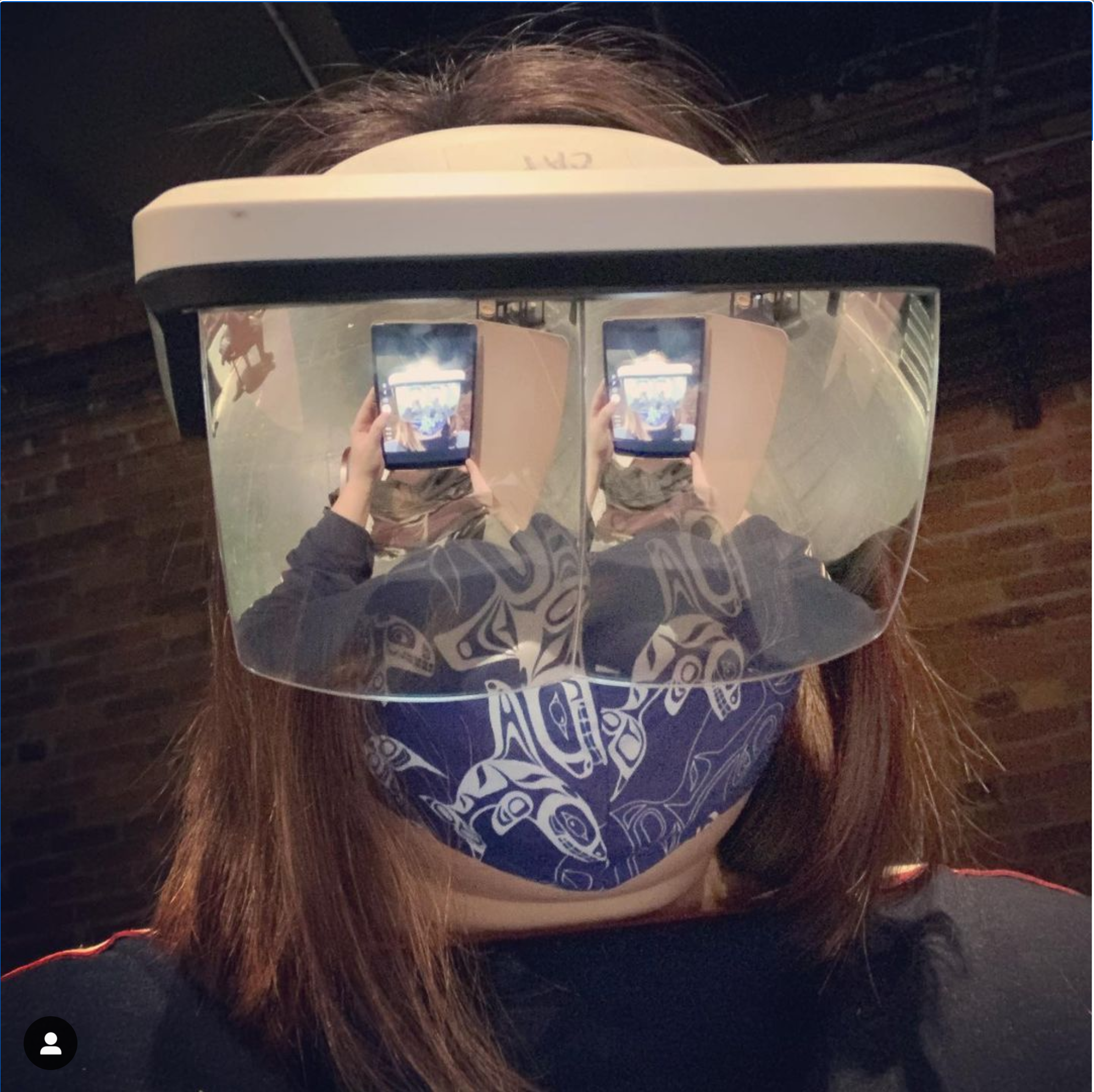 A technician wears a VR headset with reflective lenses while looking at a mobile device. The reflection of the device is visible on the visor forming a video loop.